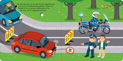 Gezeigt wird eine Innen- oder Zusatzansicht von „Mein blinkendes Soundbuch – Im Einsatz“. Die Illustration zeigt eine Szene mit einem roten Auto, das von der Straße abgekommen ist. Ein Polizist in blauer Uniform steht auf der Straße, während ein Motorradpolizist mit Helm auf einem Motorrad steht. Gelbe Absperrungen markieren den Unfallbereich. Die Umgebung ist grün mit Bäumen, und im Hintergrund ist ein weiterer blauer Wagen zu sehen. Die Schrift ist klar und kindgerecht, der Text...