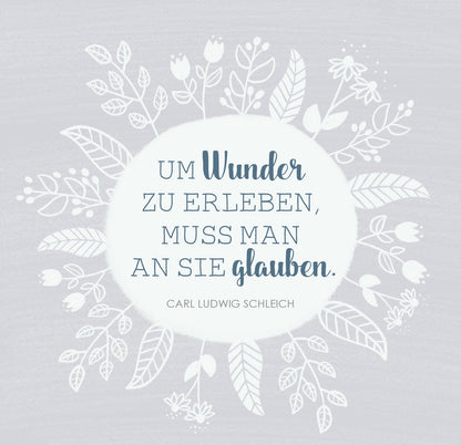 Gezeigt wird eine Innen- oder Zusatzansicht von „Das große Glück mag kleine Dinge“. Im Mittelpunkt steht ein schöner Spruch von Carl Ludwig Schleich: „Um Wunder zu erleben, muss man an sie glauben.“ Der Text ist in einer eleganten Kombinationsschrift gesetzt: „Wunder“ in geschwungener Schriftart, der Rest in klarer, gut lesbarer Typografie. Umrahmt wird der Text von filigranen, weißen Blumenelementen auf einem sanften grauen Hintergrund.