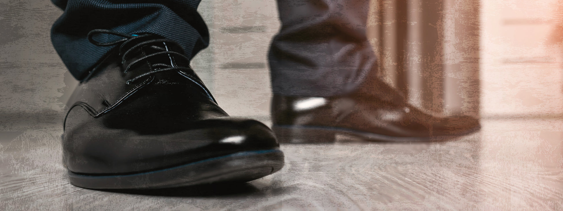 Gezeigt wird eine Innen- oder Zusatzansicht von „Escape Room. Gefangen im Schnee“. Die Abbildung zeigt die Füße eines Menschen in eleganten, schwarzen Schuhen, der auf einem hellen Holzboden steht. Die Hosenbeine sind dunkelblau und durch den klaren Fokus auf die Schuhe wirkt die Szene leicht geheimnisvoll. Die Farben sind insgesamt gedeckt, was zur spannungsgeladenen Atmosphäre des Escape Rooms beiträgt.