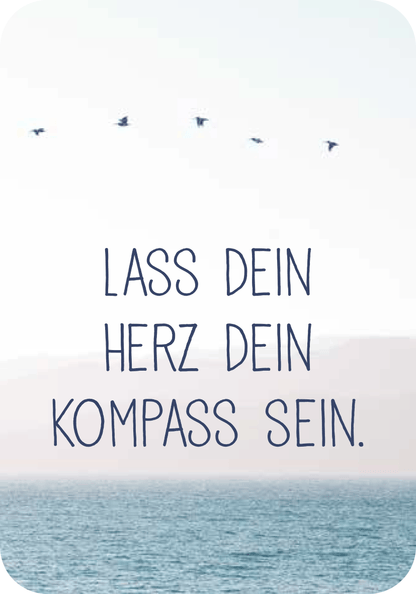 Gezeigt wird eine Innen- oder Zusatzansicht von „Achtsamkeit für die Fische“. Die Darstellung zeigt eine sanfte, bläuliche Landschaft mit dem Meer im Vordergrund und einem hellen Himmel. Vögel fliegen in einer lockeren Formation. In einer klaren, verspielten Schrift steht der Satz „LASS DEIN HERZ DEIN KOMPASS SEIN.“ in dunkler, kontrastierender Farbe, die sich harmonisch in die ruhige, naturnahe Farbpalette einfügt.