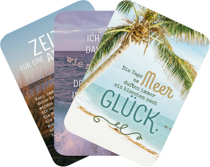 Gezeigt wird eine Innen- oder Zusatzansicht von „Meermomente“. Die Ansicht zeigt drei Karten mit unterschiedlichen Farben und Schriftzügen. Eine Karte enthält den Text „ZEIT für eine Auszeit“ in hellen, sanften Tönen, während eine andere den Satz „Die Tage am Meer sind immer ein bisschen nach GLÜCK“ in goldener, geschwungener Schrift präsentiert. Die dritte Karte hat einen zarten Farbverlauf und vermittelt eine entspannende Atmosphäre, unterstrichen durch visuelle Elemente...