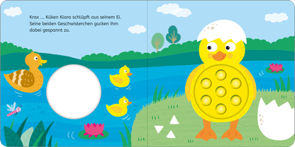 Gezeigt wird eine Innen- oder Zusatzansicht von „Mein erstes Pop-it-Buch – Küken Klara“. Die bunte Illustration zeigt Küken Klara, das aus einem Ei schlüpft, umgeben von zwei Geschwistern. Im Hintergrund erstreckt sich ein blauer See mit grünen Wiesen und bunten Blumen. Die Verwendung von leuchtenden Farben wie Gelb, Blau und Grün schafft eine fröhliche Atmosphäre. Die Schrift ist klar und gut lesbar, mit einfachem, kindgerechtem Text.