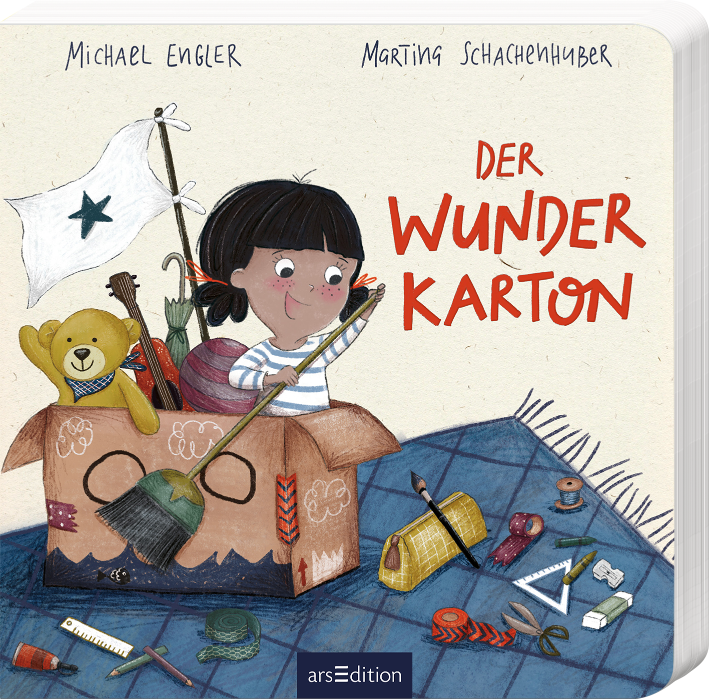 Das Buchcover zeigt ein liebevoll illustriertes Mädchen mit schwarzem Haar, das freudig aus einem großen, offenen Karton blickt. Der Karton ist gefüllt mit verschiedenen bunten Materialien, darunter ein Teddybär, eine Pinsel und andere Bastelutensilien. Über dem Mädchen weht eine kleine weiße Flagge mit einem schwarzen Stern. Die Schriftzüge „DER WUNDER KARTON“ sind in auffälligem Rot gestaltet. Oben stehen die Namen der Autoren: Michael Engler und Marting Schachenhuber. Ganz unten...