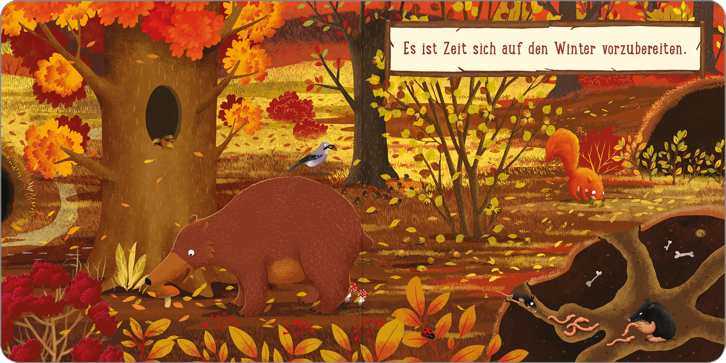 Gezeigt wird eine Innen- oder Zusatzansicht von „Ein Tag im Wald: Kleines Eichhörnchen“. Die Illustration zeigt eine herbstliche Waldlandschaft mit leuchtend orangefarbener, roter und goldener Blattfärbung. Im Vordergrund ist ein bärenförmiger Charakter zu sehen, der mit einem Baumstamm beschäftigt ist. Ein Eichhörnchen und ein Vogel sind ebenfalls abgebildet. Am oberen Rand befindet sich ein handschriftlich wirkender Text: „Es ist Zeit sich auf den Winter vorzubereiten“. Die...
