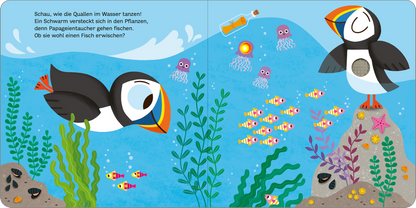 Gezeigt wird eine Innen- oder Zusatzansicht von „Mein blinkendes Soundbuch – Am Meer“. Die Illustration zeigt eine lebendige Unterwasserwelt mit verschiedenen Meeresbewohnern, darunter ein fröhlicher Papageientaucher und bunte Fische. Die Farben sind leuchtend und vielfältig mit Blau- und Grüntönen, die das Wasser und die Pflanzen darstellen. Der Text ist in einer verspielten, gut lesbaren Schriftart gehalten und ermutigt zur Interaktion mit den Abbildungen.