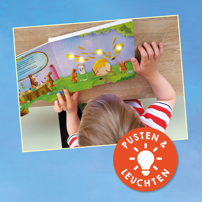Gezeigt wird eine Innen- oder Zusatzansicht von „Mein liebstes Pustebuch – Hallo Frühling!“. Die Illustration zeigt ein fröhliches, buntes Frühlingsmotiv mit Tieren und bunten Blumen auf einer grünen Wiese. Eine offene Buchseite mit textuellen Elementen in klarer, gut lesbarer Schrift auf blauen Hintergrund. Ein hervorstechendes orangefarbenes Symbol mit der Aufschrift „PUSTEN &amp; LEUCHTEN“ wird angezeigt, was auf die interaktive Funktion des Buches hinweist.