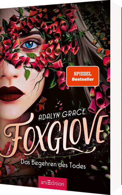 Das Buchcover zeigt das Gesicht einer Frau mit intensiven blauen Augen und einem geheimnisvollen, leicht melancholischen Ausdruck. Ihr Gesicht ist teilweise von einer dichten Blütenpracht in verschiedenen Rot- und Grüntönen umgeben. Der Titel „Foxglove“ ist in geschwungener, eleganter Schrift in beige gehalten, während der Untertitel „Das Begehren des Todes“ in einer sanften, leichteren Schrift darunter steht. Oben rechts befindet sich ein „SPIEGEL Bestseller“-Button. Ganz unten...