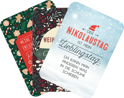 Gezeigt wird eine Innen- oder Zusatzansicht von „Einatmen. Ausrasten. Weihnachten.“. Die Ansicht zeigt drei festliche Karten mit unterschiedlichen Motiven. Die linke Karte ist in Grün mit weihnachtlichen Motiven wie Lebkuchen und Tannen. Die mittlere Karte hat ein dunkles Hintergrundmuster mit roten, grünen und weißen Elementen. Die rechte Karte ist hellblau mit einem Weihnachtsmann-Hut und roter Schrift: „DER NIKOLAUSTAG IST MEIN LIEBLINGSTAG. DA KANN MAN ANDEREN WAS IN DIE SCHUHE...
