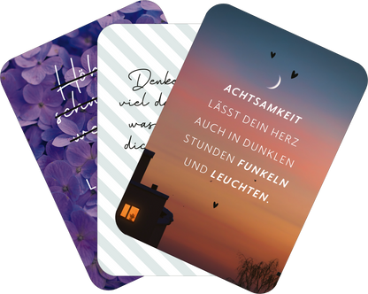Gezeigt wird eine Innen- oder Zusatzansicht von „Mini-Coach. Willkommen, Achtsamkeit!“. Die Ansicht zeigt drei Karten übereinander. Die obere Karte hat einen tiefen Lilaton mit Blumenmuster und handschriftlichem Text. Die mittlere Karte ist in einem hellen Streifenmuster gehalten, in Schwarz steht der Spruch „Denk daran, viel mehr, als du denkst, ist möglich“. Die untere Karte zeigt einen sanften Sonnenuntergang mit dem Text „ACHTSAMKEIT LÄSST DEIN HERZ AUCH IN DUNKLEN STUNDEN...