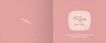 Gezeigt wird eine Innen- oder Zusatzansicht von „Happy Birthday – Alles Gute!“. Die doppelseitige Ansicht präsentiert einen sanften, rosa Hintergrund mit einer dezenten, strukturierten Optik. Links steht eine filigrane weiße Illustration einer Pflanze. Rechts befindet sich in einem abgerundeten, hellen Rahmen der Text „Offne diese Seite,“ in eleganter, goldfarbener Schrift, darunter steht in klarer, weißer Schrift „wenn du eine Portion gute Laune gebrauchen kannst…“.