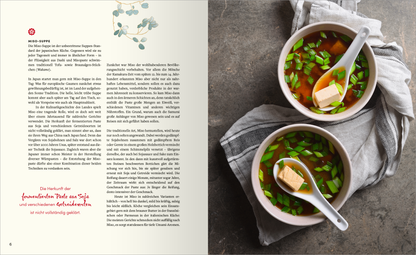 Gezeigt wird eine Innen- oder Zusatzansicht von „Sehnsucht nach Japan“. Die Seite zeigt zwei Schalen mit Miso-Suppe, die reichlich mit frischen Kräutern garniert sind, auf einem rustikalen Tisch. Der Hintergrund ist in dezenten Grautönen gehalten, während die Schalen in sanften Erdtönen strahlen. Links befindet sich ein beschreibender Text in einer eleganten serifenlosen Schrift. Ein rotes Zitat hebt sich visuell ab und rundet das harmonische Layout stimmig ab.