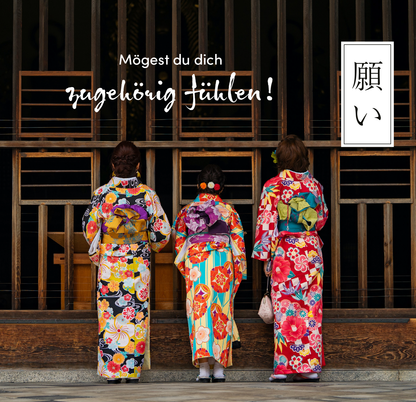 Gezeigt wird eine Innen- oder Zusatzansicht von „Sei gut zu dir“. Die Szene zeigt drei Frauen in farbenfrohen Kimonos, die lebendige Blumenmuster und kräftige Farben wie Rot, Blau und Gelb aufweisen. Sie stehen Rücken an Rücken und blicken in eine Art Innenraum. Über ihnen schwebt der Schriftzug „Mögest du dich zugehörig fühlen!“ in einer verspielten Schriftart, während auf der rechten Seite ein minimalistisches, japanisches Schriftzeichen in einem weißen Kasten zu sehen ist.