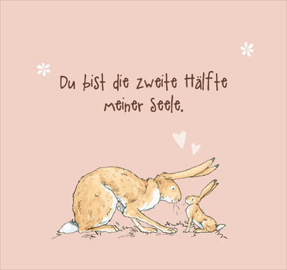 Gezeigt wird eine Innen- oder Zusatzansicht von „Bis zum Mond und wieder zurück – so sehr liebe ich dich!“. Die Illustration zeigt einen großen und einen kleinen Hasen auf einem sanft rosa Hintergrund. Über ihnen steht der geschriebene Text „Du bist die zweite Hälfte meiner Seele“ in einer verspielten, braunen Schriftart. Kleine, weiße Blumen und zarte Herzen umrahmen das Bild, was eine liebevolle und freundliche Atmosphäre schafft.