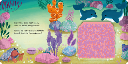 Gezeigt wird eine Innen- oder Zusatzansicht von „Klapp auf! Wo verstecken sich die Meerestiere?“. Die Illustration zeigt zwei Delfine in einem farbenfrohen Unterwasserbereich, umgeben von verschiedenen Meerespflanzen und Korallen. Dominante Farben sind Blau, Grün, Orange und Lila. Links sind ein Krebs und Muscheln abgebildet, während auf der rechten Seite eine interaktive Fläche mit einem pinken Muster für Clownfische zu sehen ist. Der Text ist in einer freundlichen, verspielten Schrift...