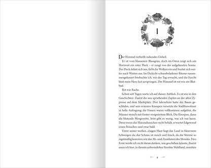 Gezeigt wird eine Innenansicht von „The North Wind – Reich aus Eis und Schatten“. Die Seite zeigt einen weißen Hintergrund mit linksseitigem Text in schwarzer Serifenschrift, der sich fließend über die Seite verteilt. Oben ist ein ornamental gestalteter Anfangsbuchstabe zu sehen, umrahmt von dekorativen Elementen. Diese sind in einem sanften Grau gehalten, was eine harmonische Verbindung zur Schrift bildet. Insgesamt vermittelt die Gestaltung eine klare und ansprechende Lesbarkeit.