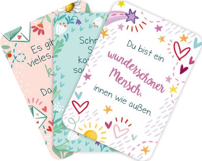 Gezeigt wird eine Ansicht von drei gefächerten Karten aus der Kartenbox „Du bist genau richtig! – 50 Karten für dich“. Die Karten präsentieren fröhliche, bunte Designs mit sanften Farben wie Türkis, Rosa und weiß. Jede Karte enthält einen Spruch in einer handschriftlich anmutenden Typografie in verschiedenen Stilen. Illustrationen von Herzen, Sonnen und floralen Elementen umrahmen die Texte und verleihen den Karten eine einladende und positive Ausstrahlung.