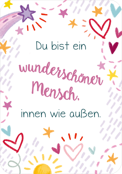 Gezeigt wird eine Innenansicht von „Du bist genau richtig! – 50 Karten für dich“. Die Karte hat einen weißen Hintergrund und ist mit bunten Illustrationen wie Herzen, Sternen und einer Sonne verziert. In der Mitte steht der Text „Du bist ein wunderschöner Mensch, innen wie außen.“.