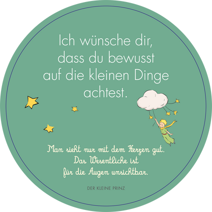 Gezeigt wird eine Innen- oder Zusatzansicht von „Adventskalender in der Dose. Der Kleine Prinz. 24 liebe Wünsche im Advent“. Die runde Ansicht hat einen mintgrünen Hintergrund, auf dem in großer, klarer Schrift der Wunsch steht: „Ich wünsche dir, dass du bewusst auf die kleinen Dinge achtest.“ Unterhalb befindet sich ein Zitat in kleinerer Schrift, versehen mit einer Illustration des kleinen Prinzen, der inmitten von Sternen und einer Wolke schwebt.