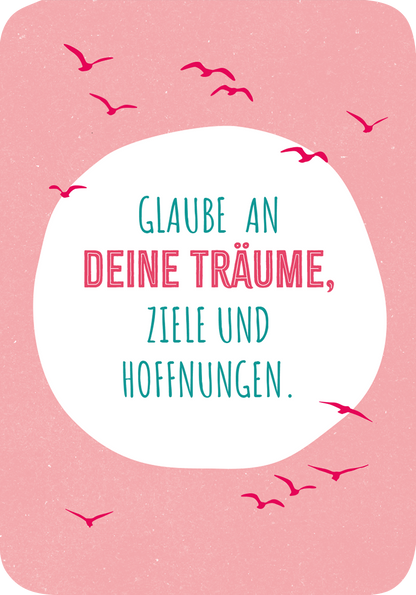Gezeigt wird eine Innen- oder Zusatzansicht von „Glückskärtchen zur Jugendweihe“. Der Hintergrund ist in einem sanften Rosa gehalten, umrahmt von einem weißen Oval. In der Mitte steht der Text „Glaube an DEINE TRÄUME, ZIELE UND HOFFNUNGEN.“ in einer verspielten, modernen Schrift. Der Haupttext ist aquamarinfarben und die hervorgehobenen Wörter sind in leuchtendem Pink gehalten. Um den Text fliegen stilisierte, graue Vögel, die dem Design eine freundliche Dynamik verleihen.