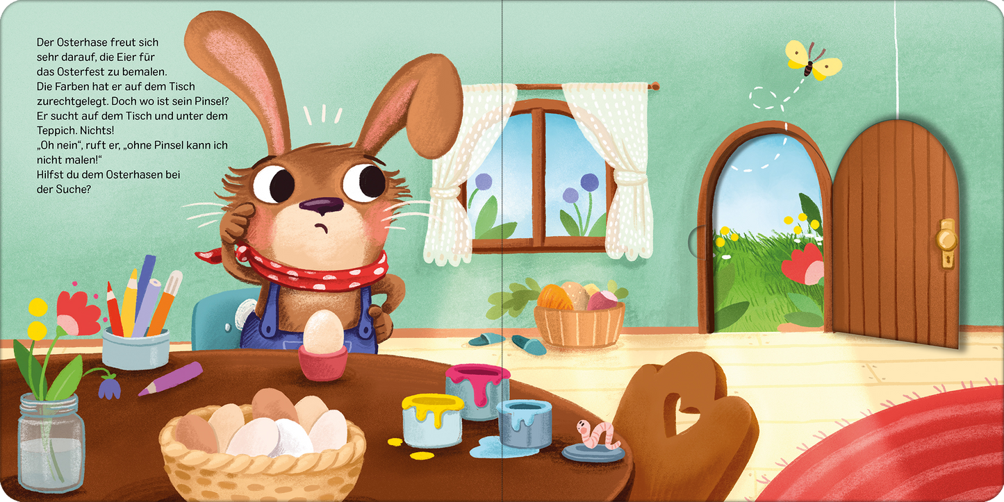 Gezeigt wird eine Innen- oder Zusatzansicht von „Der vergessliche Osterhase“. Der Osterhase sitzt an einem holzfarbenen Tisch, umgeben von bemalten Eiern und Farbtöpfen in lebhaften Farben wie Blau, Gelb und Rot. Die Wände sind in sanftem Grün gehalten, und durch ein großes Fenster fällt Tageslicht. Ein runder Teppich in warmen Rottönen und eine offene Tür mit einer blühenden Wiese im Hintergrund schaffen eine freundliche Atmosphäre. Der Hase trägt ein rotes Halstuch und schaut...