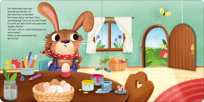 Gezeigt wird eine Innen- oder Zusatzansicht von „Der vergessliche Osterhase“. Der Osterhase sitzt an einem holzfarbenen Tisch, umgeben von bemalten Eiern und Farbtöpfen in lebhaften Farben wie Blau, Gelb und Rot. Die Wände sind in sanftem Grün gehalten, und durch ein großes Fenster fällt Tageslicht. Ein runder Teppich in warmen Rottönen und eine offene Tür mit einer blühenden Wiese im Hintergrund schaffen eine freundliche Atmosphäre. Der Hase trägt ein rotes Halstuch und schaut...
