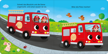 Gezeigt wird eine Innen- oder Zusatzansicht von „Tatütata, kleine Feuerwehr!“. Die doppelseitige Illustration zeigt ein fröhliches, rotes Feuerwehrfahrzeug auf einer Straße. Im Fahrzeug sitzen zwei Kinder mit roten Mützen, die begeistert in die Landschaft blicken. Umgeben ist die Szene von grünen Wiesen, bunten Blumen und einem blauen Himmel. Der Text in kindgerechter, klarer Typografie lädt zum Mitmachen ein. Die Farben sind lebhaft und ansprechend gestaltet.