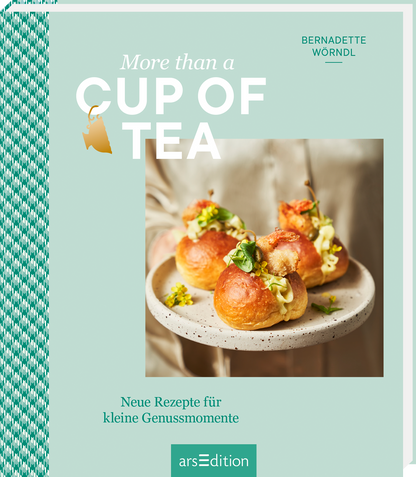 Das Buchcover zeigt eine sanfte mintgrüne Hintergrundfarbe. In der Mitte ist ein Teller mit kleinen, gefüllten Brötchen abgebildet, die mit frischen Kräutern dekoriert sind. Der Titel „More than a CUP OF TEA“ ist in großen, weißen Buchstaben gestaltet. Darüber erscheint ein kleiner, goldener Teebeutel. Am unteren Rand steht der Untertitel „Neue Rezepte für kleine Genussmomente“ in schlichter Schrift. Ganz unten mittig steht der Logoschriftzug von arsEdition.