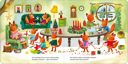 Gezeigt wird eine Innen- oder Zusatzansicht von „Mein erstes Adventskalenderbuch“. Die Szene zeigt einen gemütlichen Fuchsbaus mit warmen, waldgrünen und leuchtend roten Tönen. Mehrere Füchse in bunten Pullis sind beschäftigt: Einige basteln am Tisch, während andere mit bunten Sternen und Dekoration arbeiten. Eine große Fensteröffnung zeigt verschneite Tannenbäume. Auf dem Tisch stehen vier rote Kerzen und Bastelmaterialien sind verteilt, was eine einladende Adventsatmosphäre...