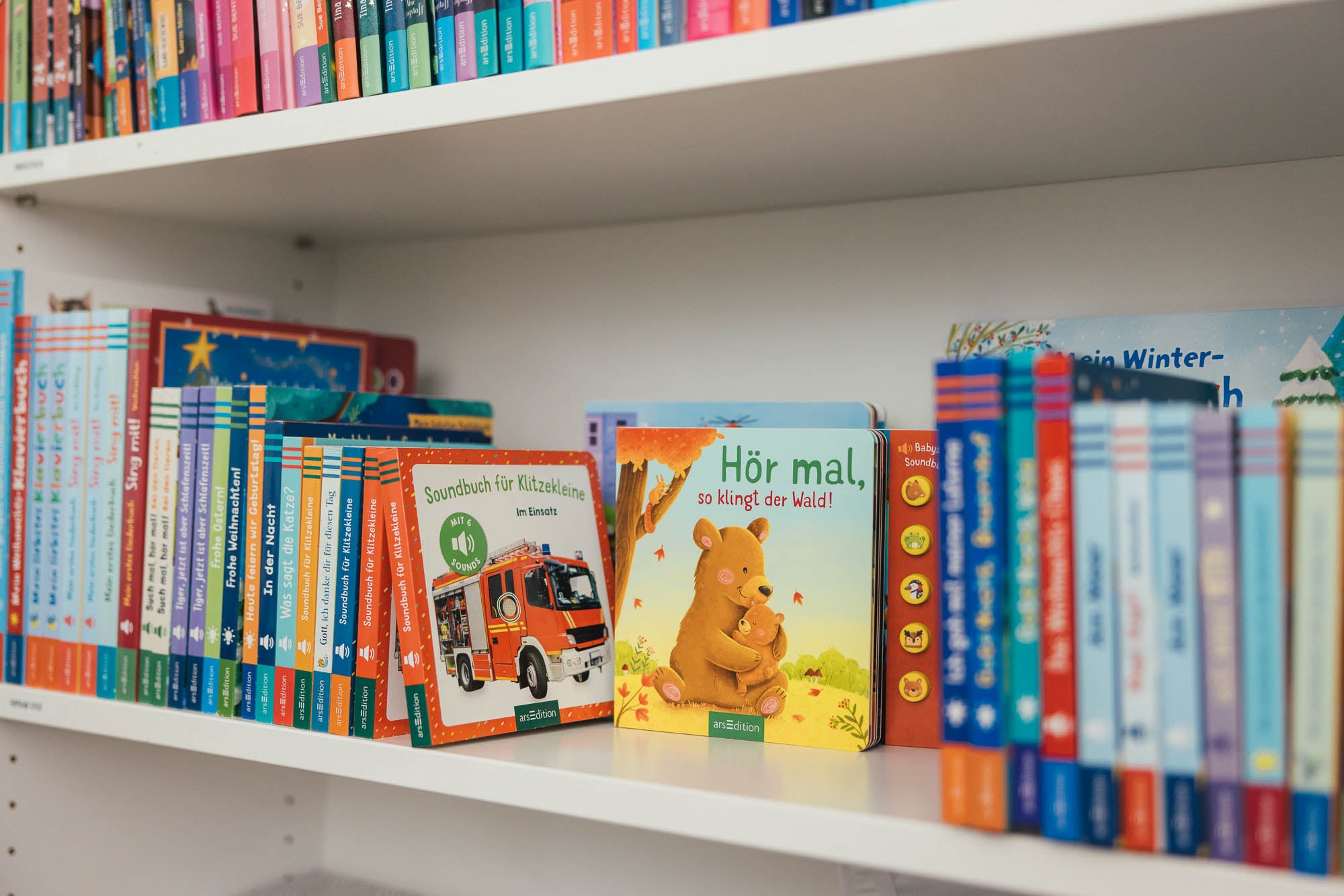 Ein Bücherregal mit einer Auswahl an Soundbüchern für Kinder des Verlags arsEdition. Es sind bunte Buchreihen mit verschiedenen Titeln sichtbar, darunter interaktive Soundbücher wie „Soundbuch für Klitzekleine – Im Einsatz“ mit einem Feuerwehrauto auf dem Cover und „Hör mal, so klingt der Wald!“ mit einem Bärenmotiv. Die Regalebenen sind dicht mit Büchern zu Themen wie Natur, Fahrzeuge und Weihnachten gefüllt.