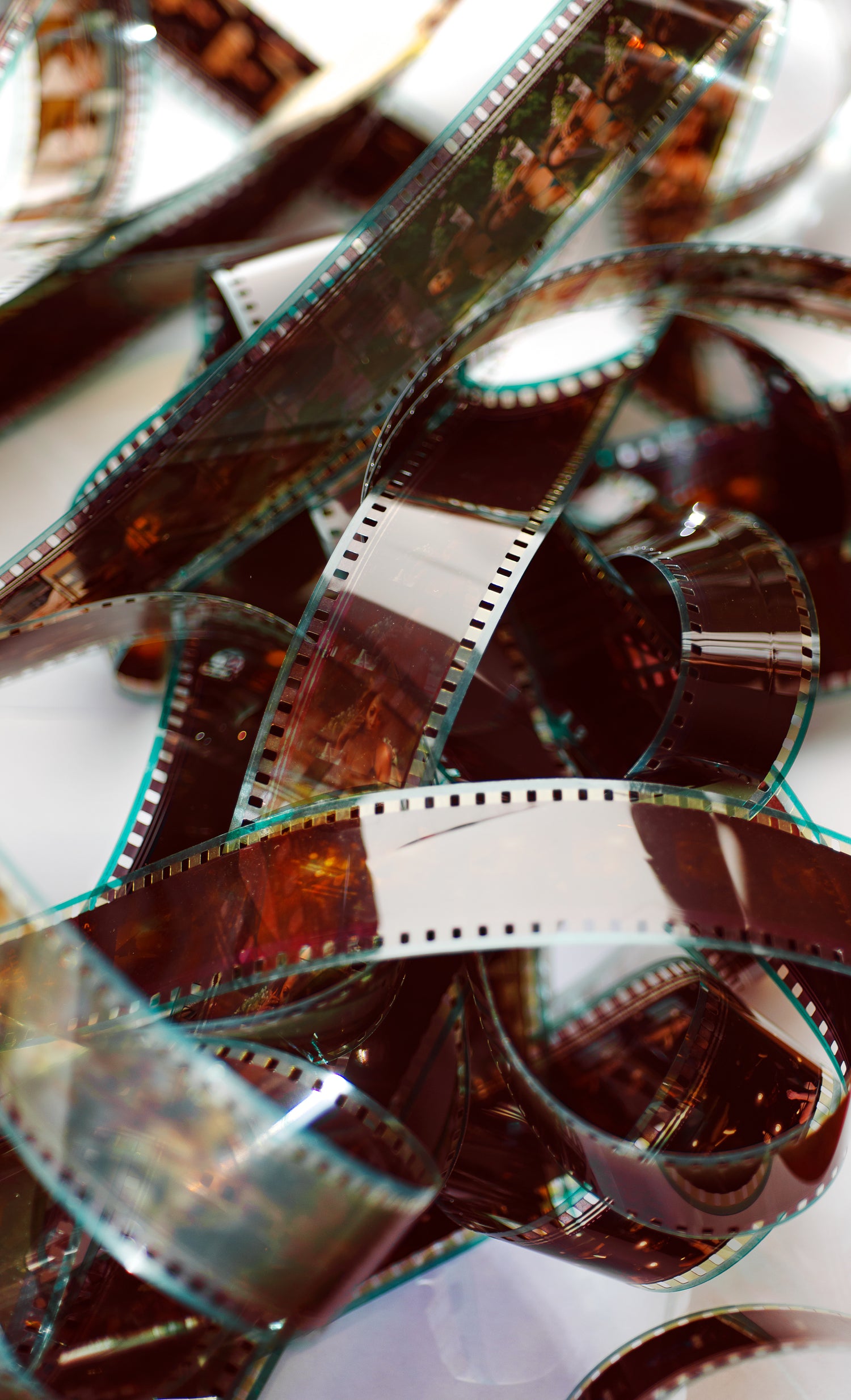 Ein Haufen ineinander verschlungener, entwickelter Filmstreifen, die mit ihren perforierten Rändern und leicht durchscheinenden Bildern auf jedem Streifen an analoge Fotografie erinnern. Die Filmstreifen sind in warmen Brauntönen gehalten und reflektieren das Licht leicht.
