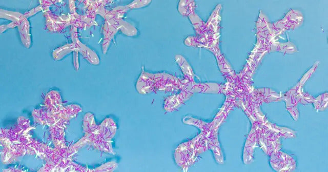 Nahaufnahme von glitzernden Schneeflocken aus Bastelmaterial auf einem hellblauen Hintergrund, verziert mit rosa und silbernem Glitzer.