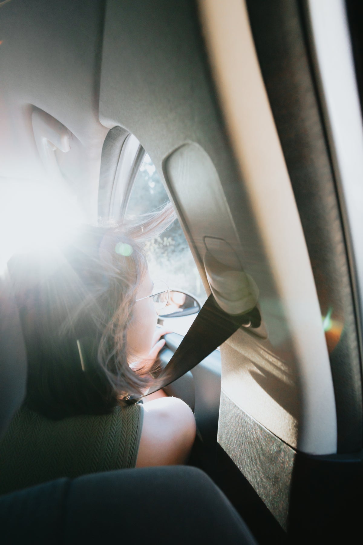 Eine weibliche Person sitzt auf der Beifahrerseite eines Autos. Sie guckt aus dem Fenster, die Sonne scheint ihr ins Gesicht.