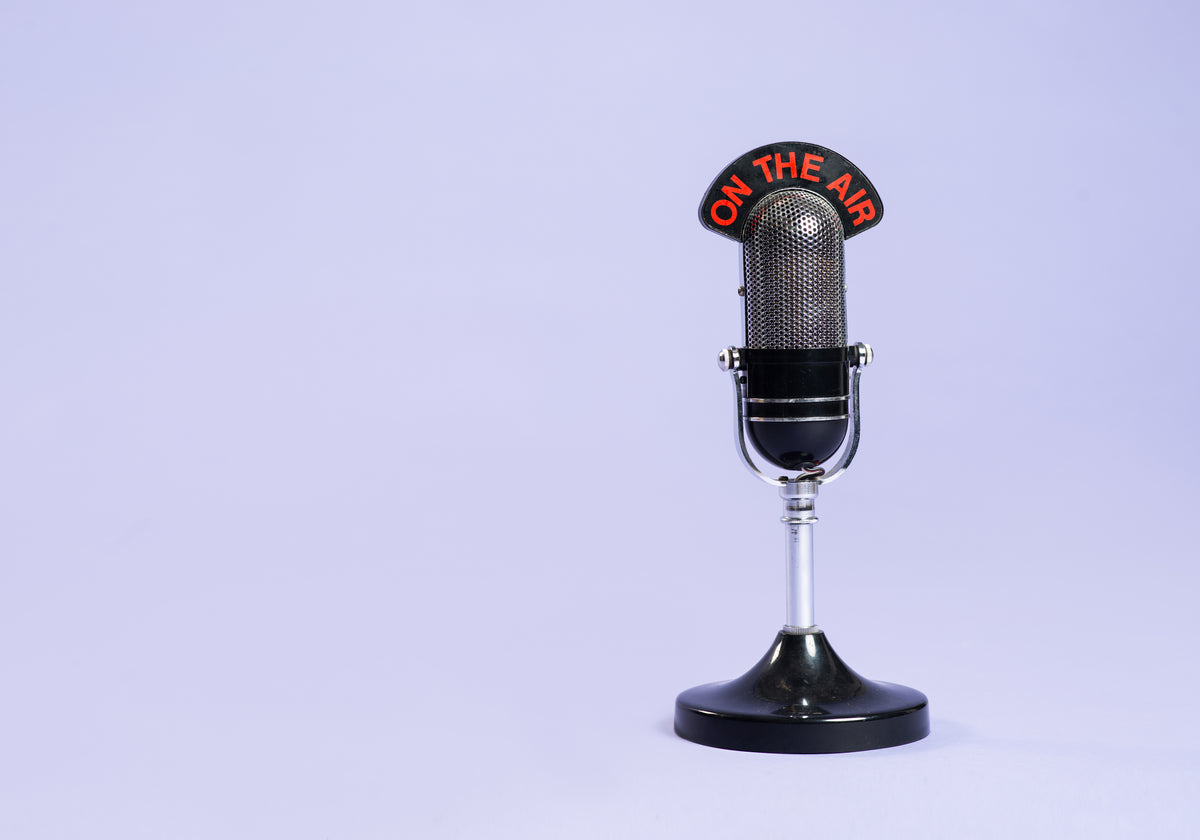 Ein Retro-Mikrofon vor lila Hintergrund. Auf dem Mikrofon steht: On the Air.